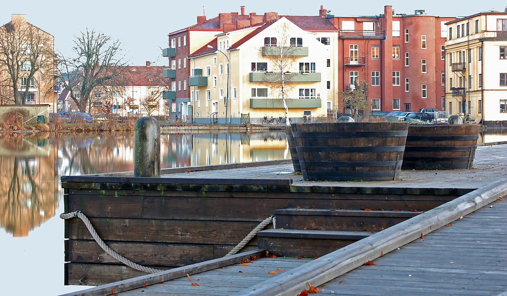 Brygga vid en lugn vattenyta med bostadshus i bakgrunden.