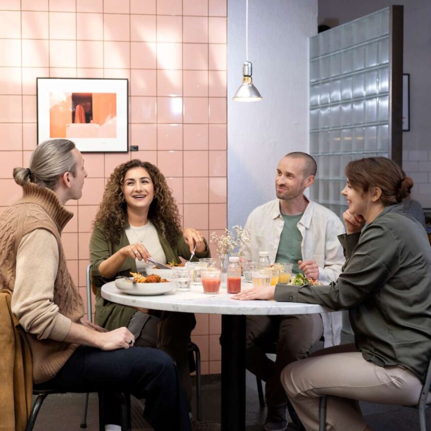 Fyra personer sitter vid ett runt bord i en modern restaurang och samtalar medan de äter.