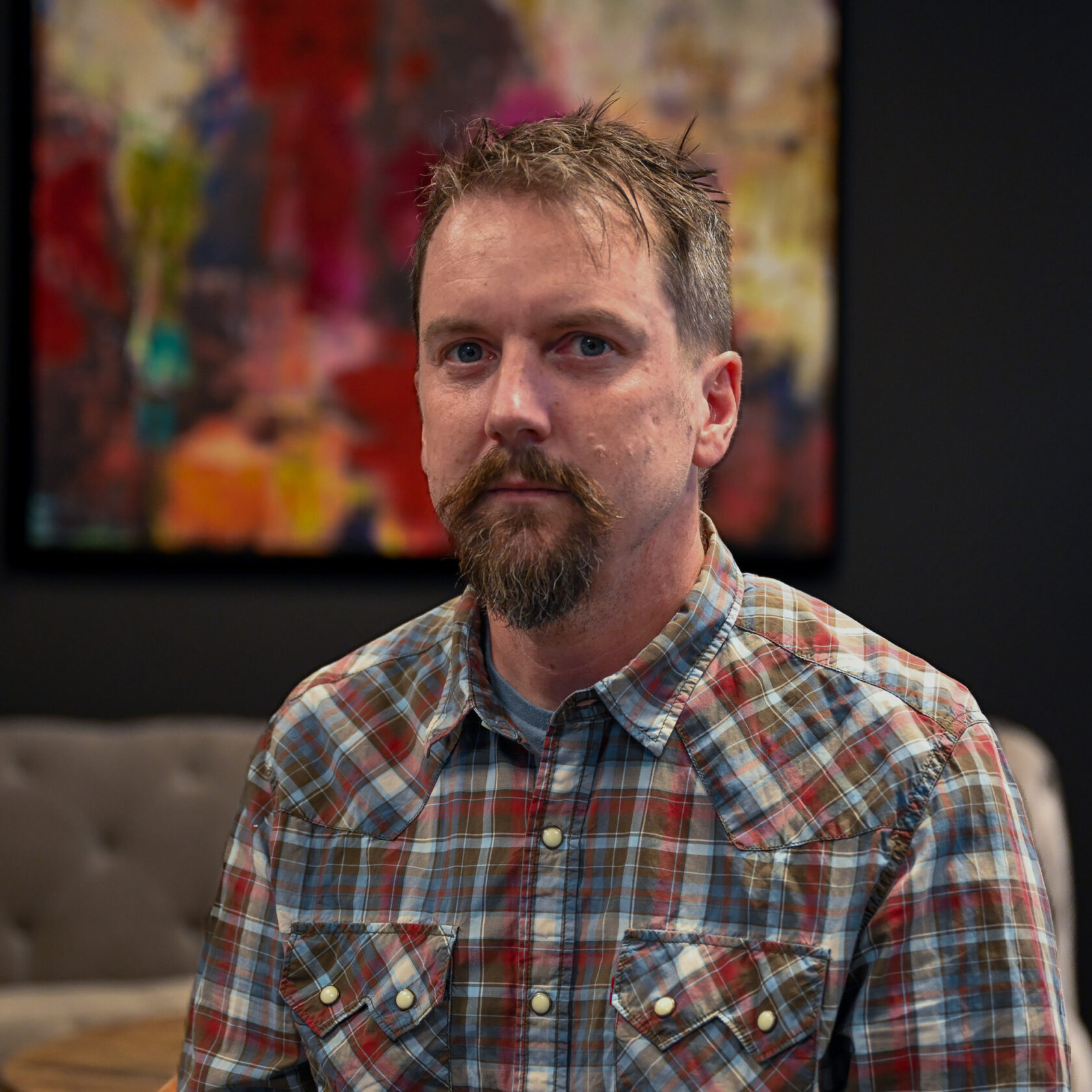 Man i rutig skjorta sitter framför en abstrakt målning.