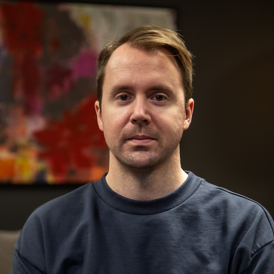 En person i en mörkblå tröja sitter framför en färgglad, abstrakt tavla.