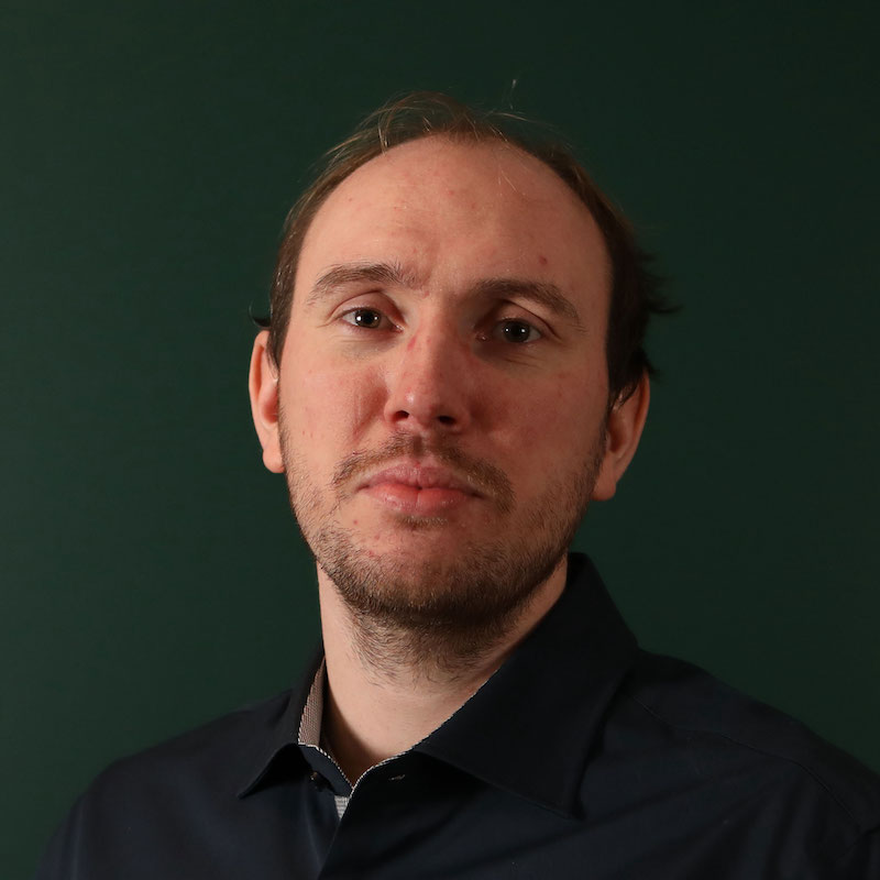 En person med skjorte foran en mørk grønn bakgrunn.