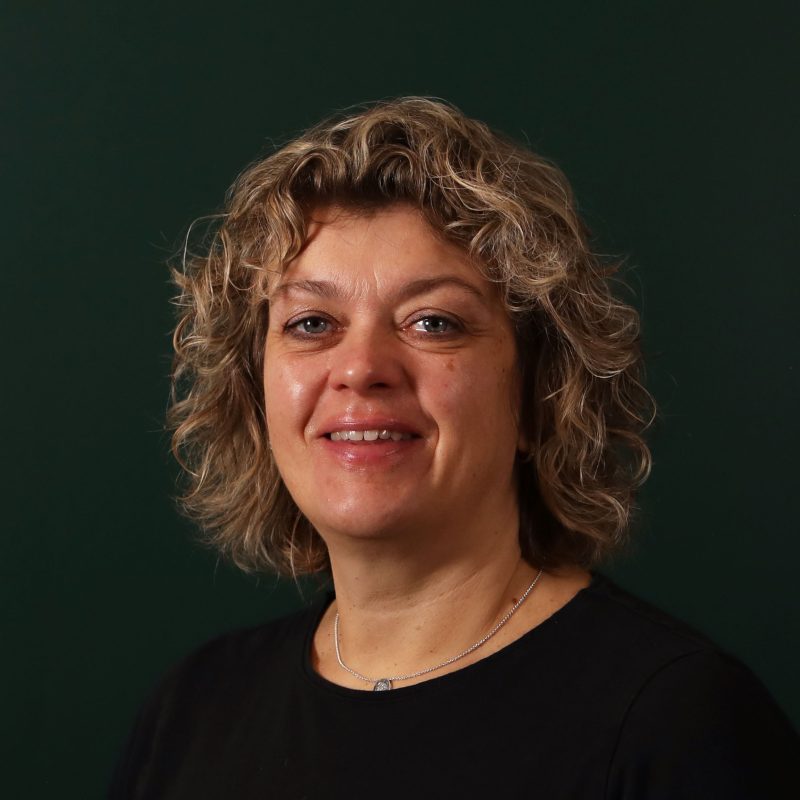 Kvinne med krøllete hår smiler foran en mørk grønn bakgrunn.