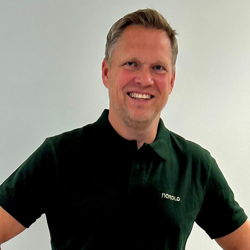 En mann med mørk grønn skjorte smiler mot kameraet.