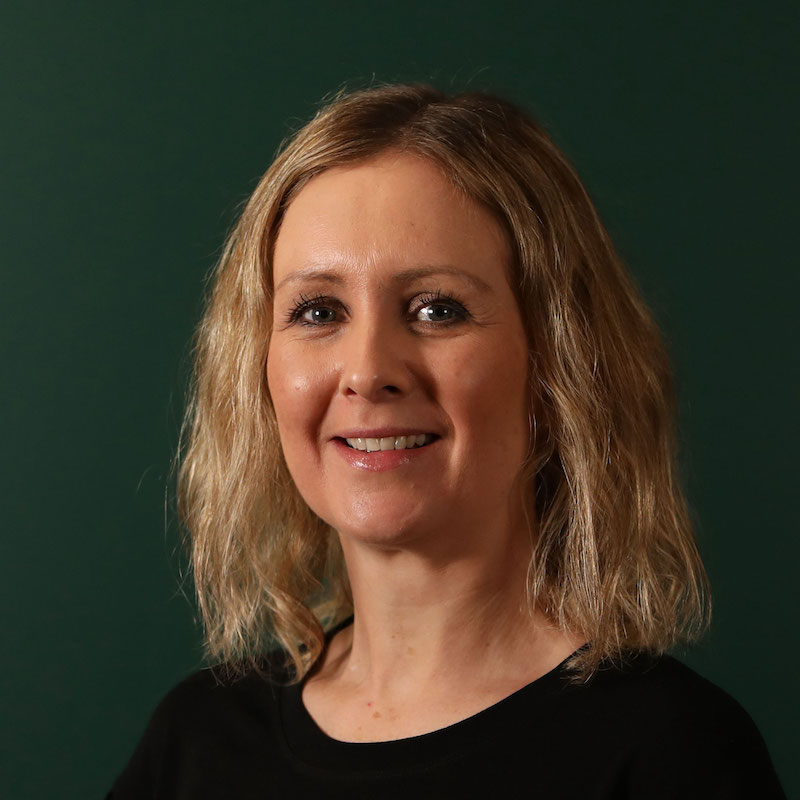 Kvinne med lyst, bølgete hår og svart topp mot grønn bakgrunn.