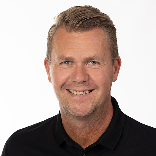 En leende man med kort hår och svart tröja mot vit bakgrund.