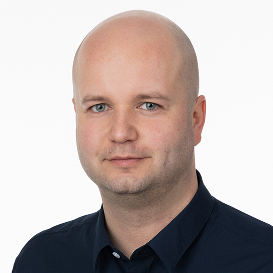 En man med rakad huvud och mörk skjorta mot vit bakgrund.
