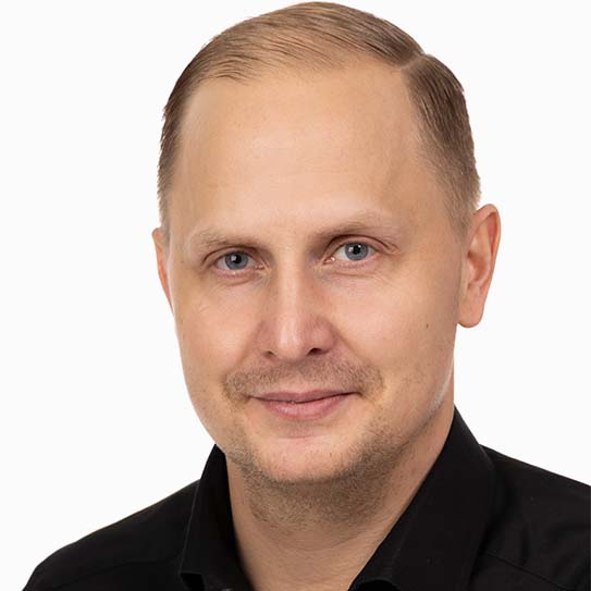 Man i svart skjorta mot vit bakgrund, leende.