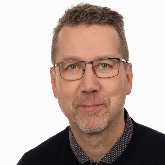 Man med glasögon och kort hår, klädd i en mörk tröja mot vit bakgrund.