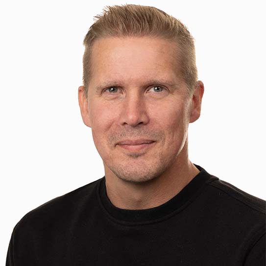 En person med kort hår och en svart tröja, mot en vit bakgrund.
