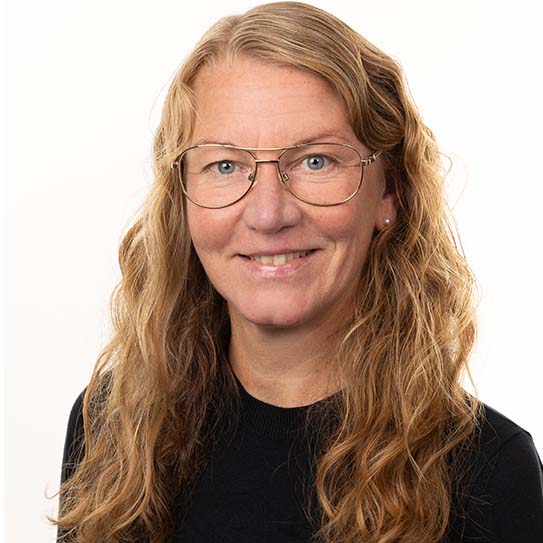 Kvinna med långt lockigt hår och glasögon, klädd i en svart tröja mot en ljus bakgrund.