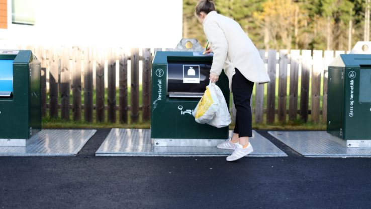 En person kaster søppel i en avfallsdunk på en gjenvinningsstasjon utendørs.